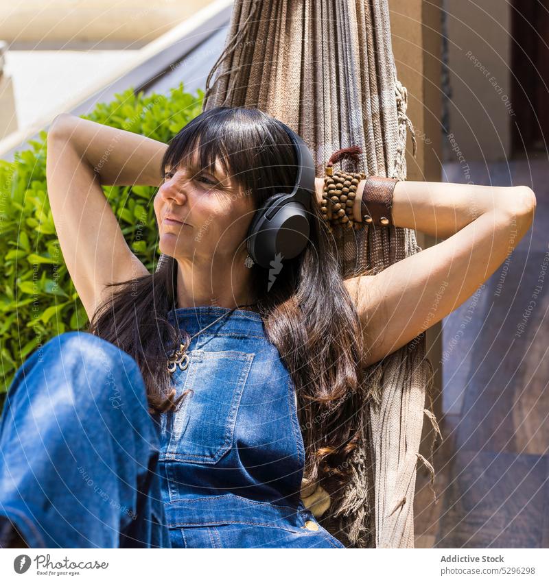 Happy woman listening to music in hammock in park headphones rest yard smile relax leisure song device happy enjoy delight casual audio wireless female positive