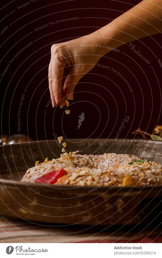 Woman pouring almonds on a Roscon de Reyes, a typical spanish christmas cake sweet food celebration dessert traditional roscon homemade baked rosca holiday