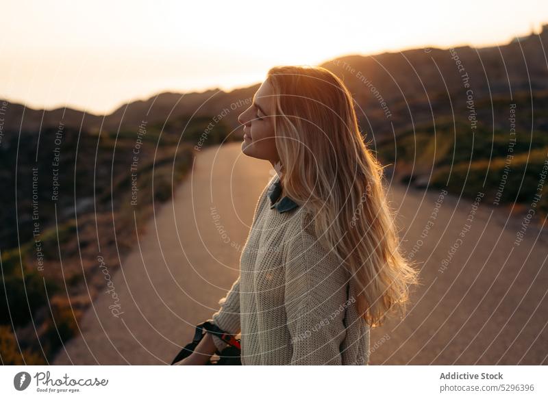 Smiling woman standing with eyes closed against mountains at sundown road sunset summer traveler picturesque leisure trip happy smile female freedom enjoy