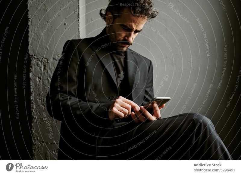 Confident man using smartphone in dark room browsing gadget chair thoughtful beard wireless gentleman serious adult male classy connection mobile online