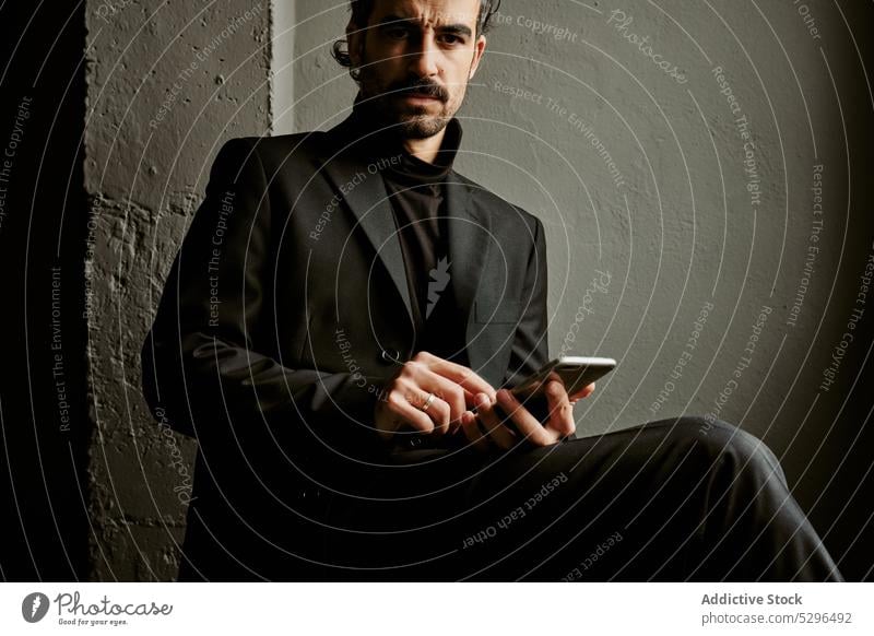 Confident man using smartphone in dark room browsing gadget chair thoughtful beard wireless gentleman serious adult male classy connection mobile online