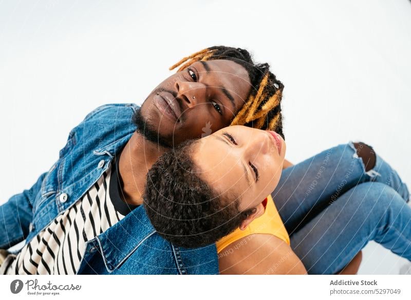 African American couple sitting close to each other in white studio relationship boyfriend girlfriend affection back to back fondness together partner love