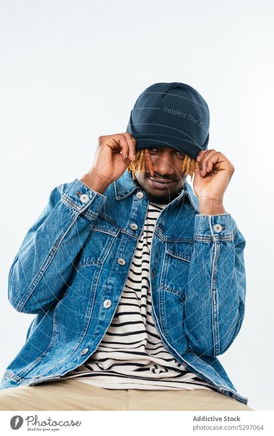 Stylish black man pulling hat on forehead positive style street style appearance denim playful studio shot dreadlocks african american ethnic mustache male