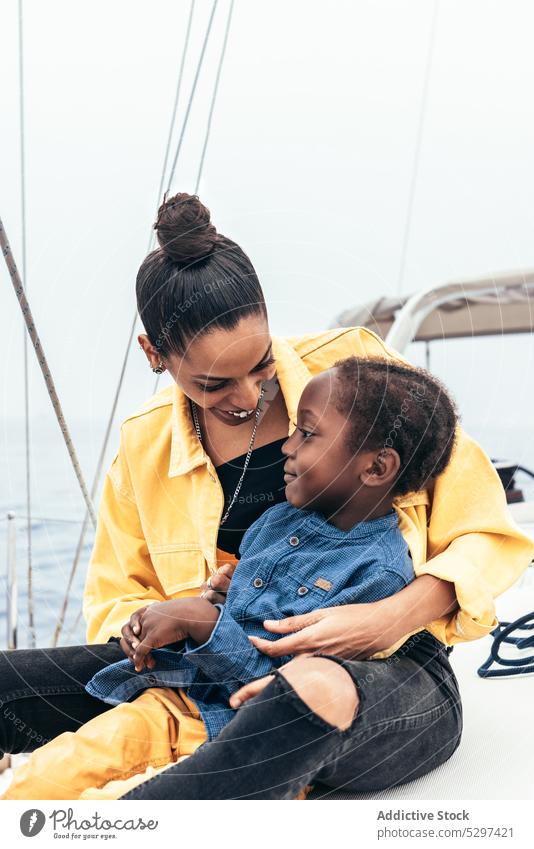 Cheerful black woman embracing son in yacht mother smile together weekend hug embrace happy boy child casual gesture sea summer parent kid glad affection