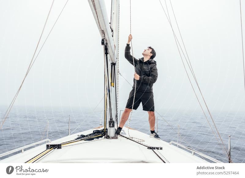 Focused man raising sail on yacht trip rope pull sea sailboat cruise transport male vessel adventure nature ocean journey traveler nautical vacation freedom