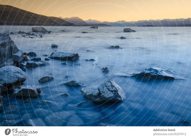 Rocky coast with rocks in lake at sunset stone rocky shore mountain sundown nature lake tekapo new zealand picturesque landscape scenic environment water