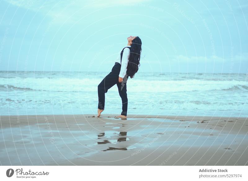 Slim woman bending back on seashore beach wave eyes closed ocean sand calm relax coast female young long hair style wavy hair nature wind water harmony seaside