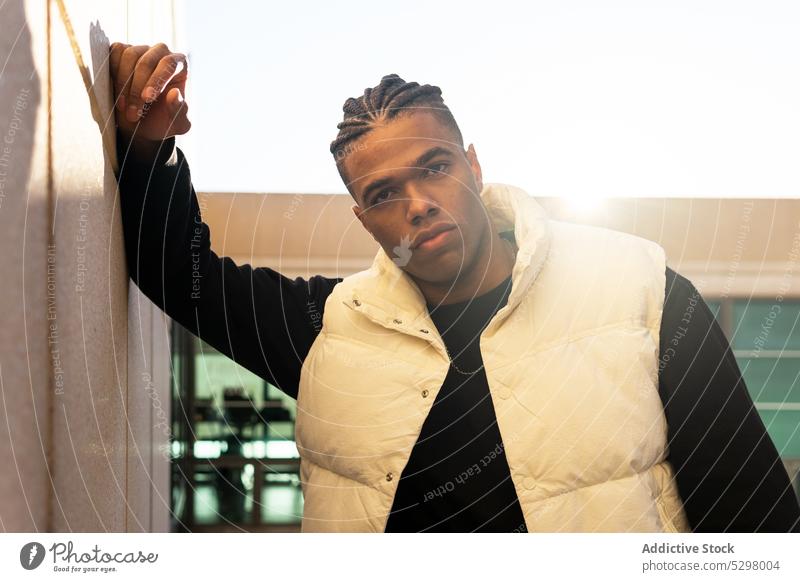 Serious black man leaning on wall on street city style building trendy confident outfit urban serious young male ethnic modern lean on dreadlocks appearance