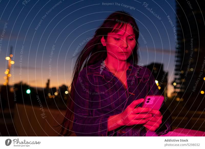 Woman using smartphone in neon light on street woman night city browsing female urban illuminate gadget mobile device dark modern connection surfing