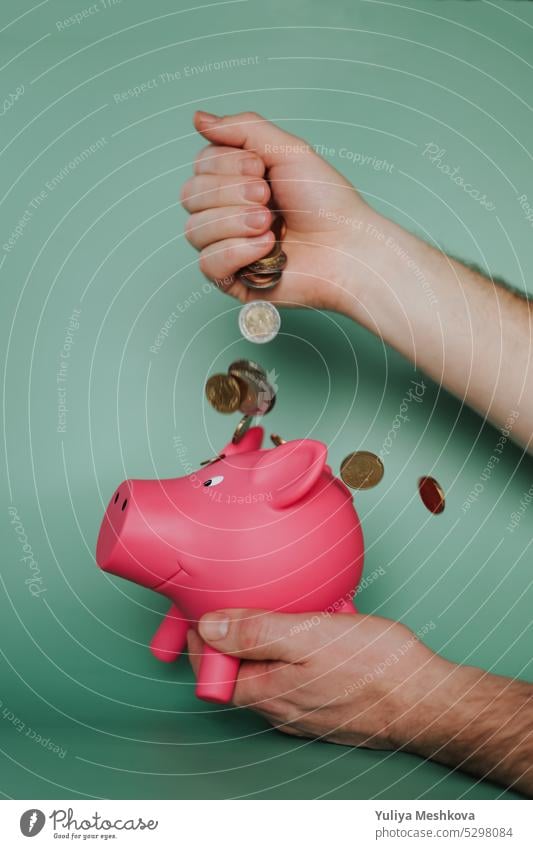 Piggy bank.Savings and spending concept.Falling euro coins from a male hand and a pink piggy bank on a green background Hand European Union money finance