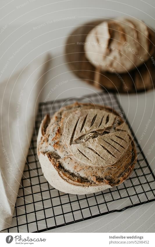 Home made sourdough bread. Resting on cooling rack and wooden board. On the left side there is a linen napkin. Minimalism in a vertical flat lay image. loaf