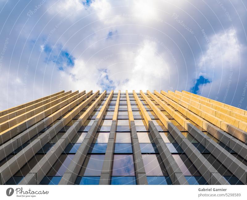 Modern building in the city of Nantes in a low-angle shot. Reflections of the sky and clouds on the building. Blue and cloudy sky in the background. Sunny.