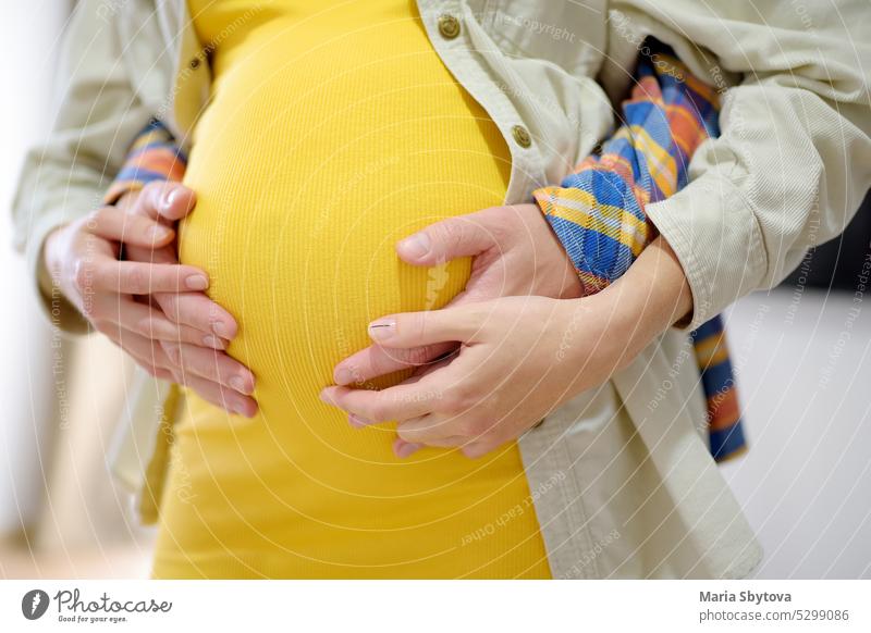 Young man holding hands on pregnant belly of his wife tummy young couple future parent woman close up closeup keep stomach care hug unrecognizable embrace