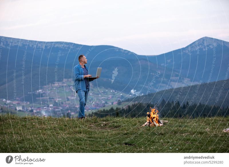 Man working outdoors with laptop standing in mountains. Concept of remote work or freelancer lifestyle. Cellular network broadband coverage. internet 5G. Hiker tourist enjoying valley view