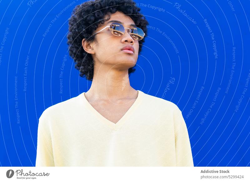 Young man in sunglasses looking away against blue background style cool color bright street male curly hair young casual modern sincere accessory joy outfit