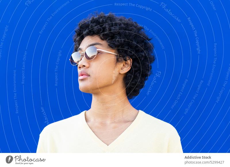 Young man in sunglasses looking away against blue background style cool color bright street male curly hair young casual modern sincere accessory joy outfit