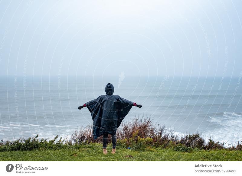 Anonymous hiker in raincoat admiring seascape woman traveler wave tourist admire nature storm stormy sky weather shore coast atmosphere ocean journey female