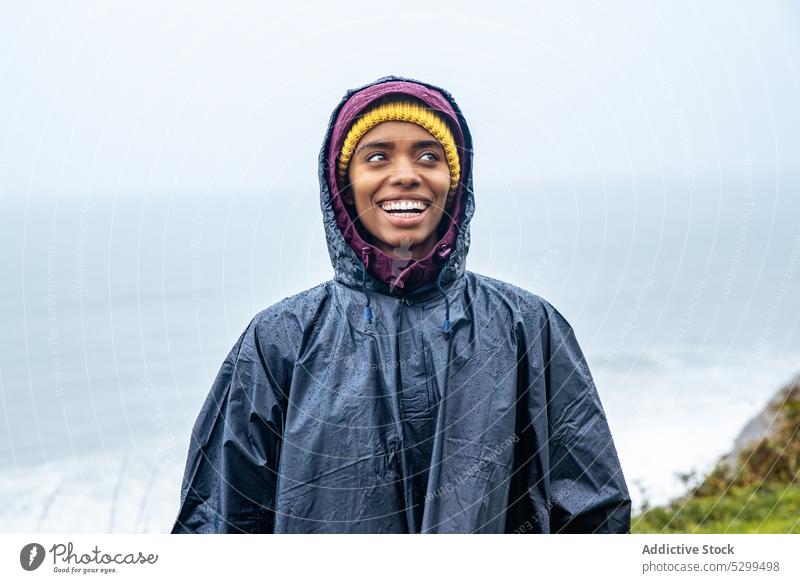 Serious woman in raincoat against ocean during trip hiker traveler vacation portrait serious tourist sea tourism nature cloudless female young journey coast