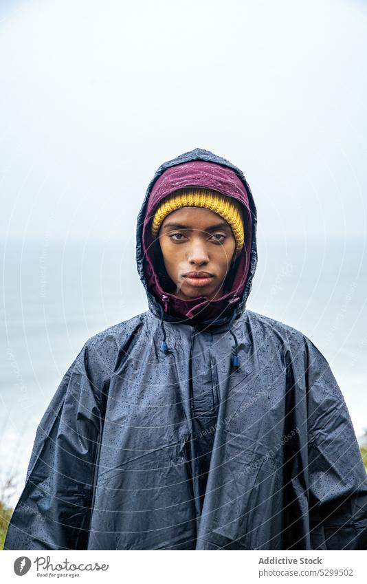 Serious woman in raincoat against ocean during trip hiker traveler vacation portrait serious tourist sea tourism nature cloudless female young journey coast