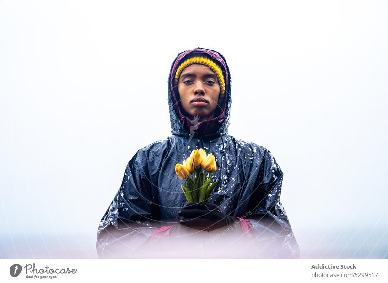 Woman in raincoat holding yellow tulips near sea woman flower confident nature bouquet season weather serious young female calm lady harmony individuality