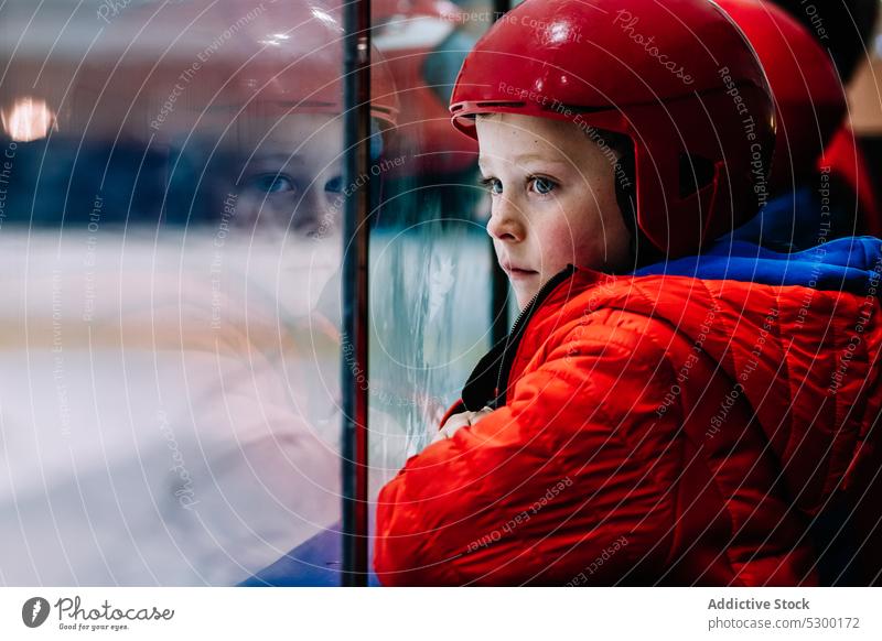 Pensive boy looking at ice rink winter kid safety thoughtful fence protect cold pensive serious helmet season child activity sport outerwear childhood frozen