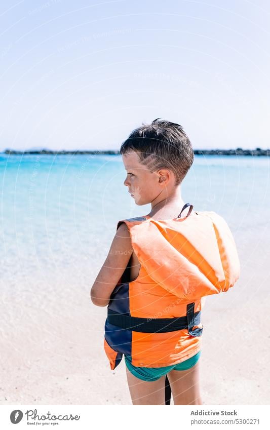 Boy in swim safety jacket while standing near sea boy beach summer seashore child kid water coast childhood ocean pleasure delight holiday seaside vacation