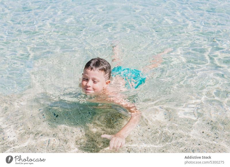 Happy boy swimming in clean water seashore resort wet hair kid beach pool recreation child childhood activity aqua holiday leisure shirtless clear ripple