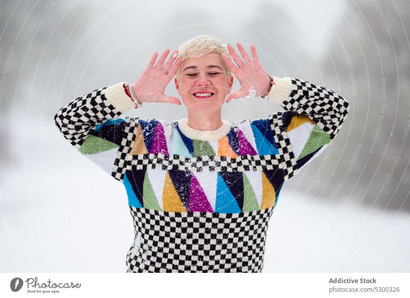 Cheerful adult woman with raised hands in snowy forest happy cheerful smile winter positive nature cold pleasure blond knitted enjoy eyes closed colorful female