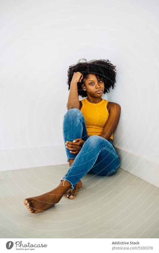 Calm black woman sitting on floor thoughtful calm pensive serious appearance curly hair hairstyle barefoot tranquil female young african american casual afro