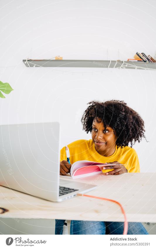 Focused black woman writing information in notebook laptop take note write student study education concentrate learn focus female young curly hair