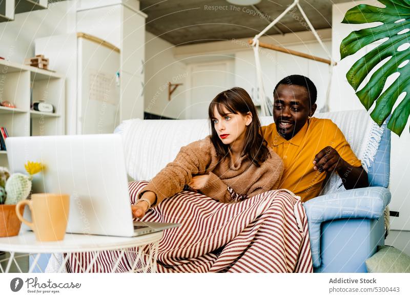 Couple using laptop in living room at home couple sofa relationship browsing together spend time diverse online multiracial multiethnic young internet device