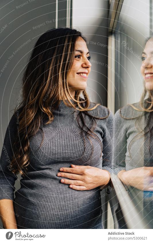 Pregnant woman standing near window caressing belly pregnant love touch belly maternity leave anticipate tranquil mother await smile female young stomach