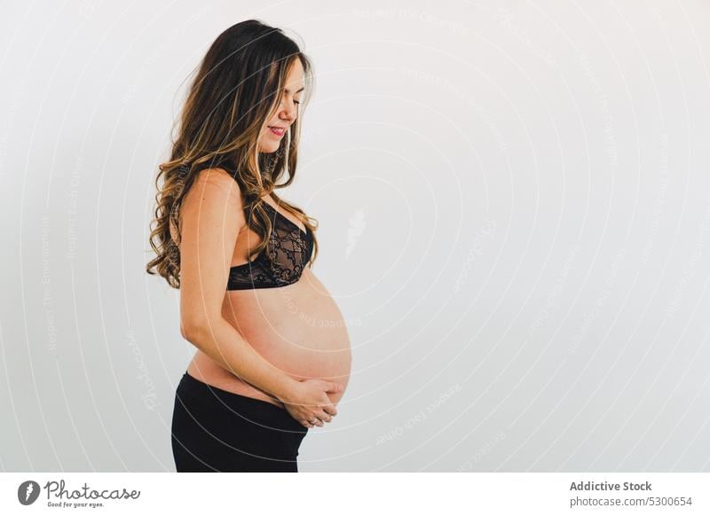 Young smiling woman carrying baby standing against white background pregnant studio shot happy maternity leave care smile love await glad caress delight