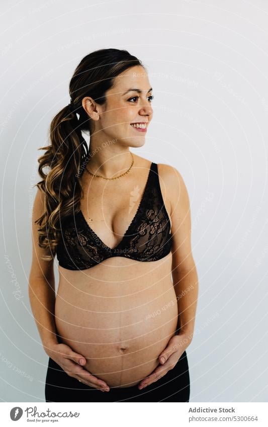 Young smiling woman carrying baby standing against white background pregnant studio shot happy maternity leave care smile love await glad caress delight