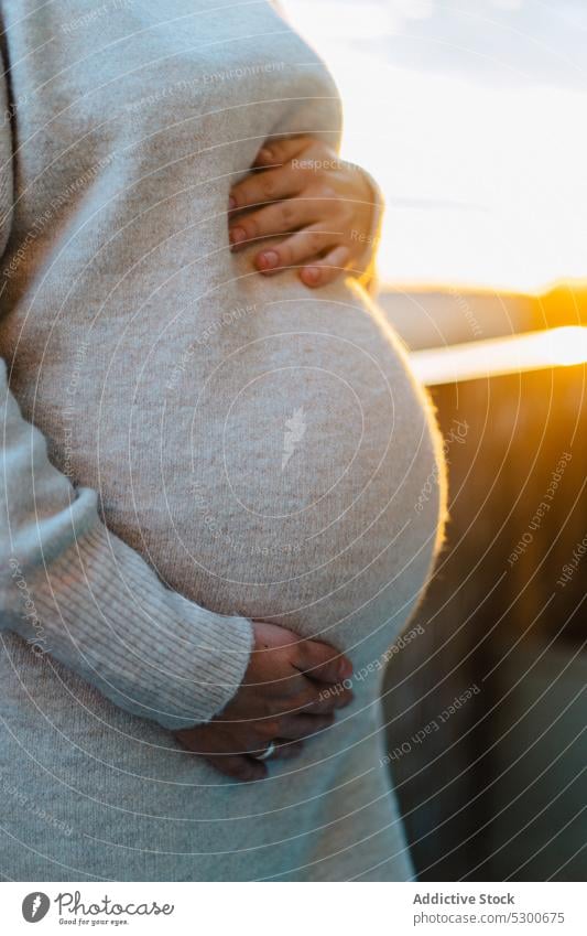 Anonymous pregnant woman hugging belly on terrace unborn baby tender love caress touch belly sunlight sunset female young anticipate maternity leave parent