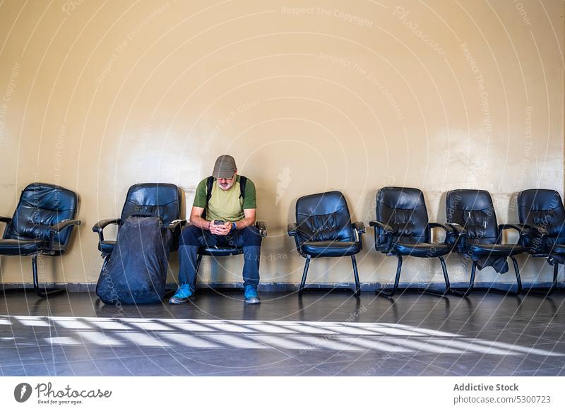 Man using cellphone in airport waiting room man smartphone traveler tourist passenger trip rest male casual browsing chair device luggage backpack sit mobile