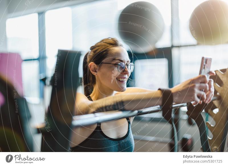 Portrait of a young woman using mobile phone in a gym wellness wellbeing bodybuilder sporty lifting biceps muscles barbell bodybuilding people muscular adult