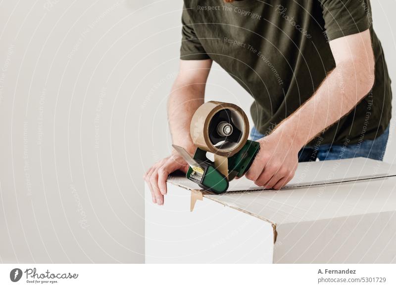 A man using a tool to pack a cardboard box with tape. Concept of packing and moving out Cardboard Cardboard box Moving (to change residence) moving day Box