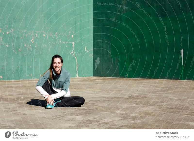 Smiling woman resting after workout on street break positive smile floor training sporty concrete ponytail female young shabby cheerful fitness happy confident