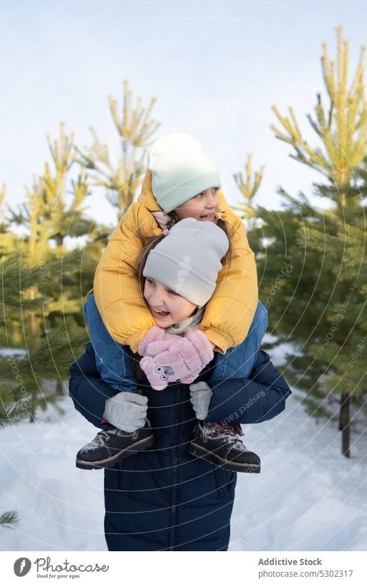 Happy sisters spending time together in winter forest sibling happy childhood piggyback cheerful walk warm clothes smile children leisure street nature adorable