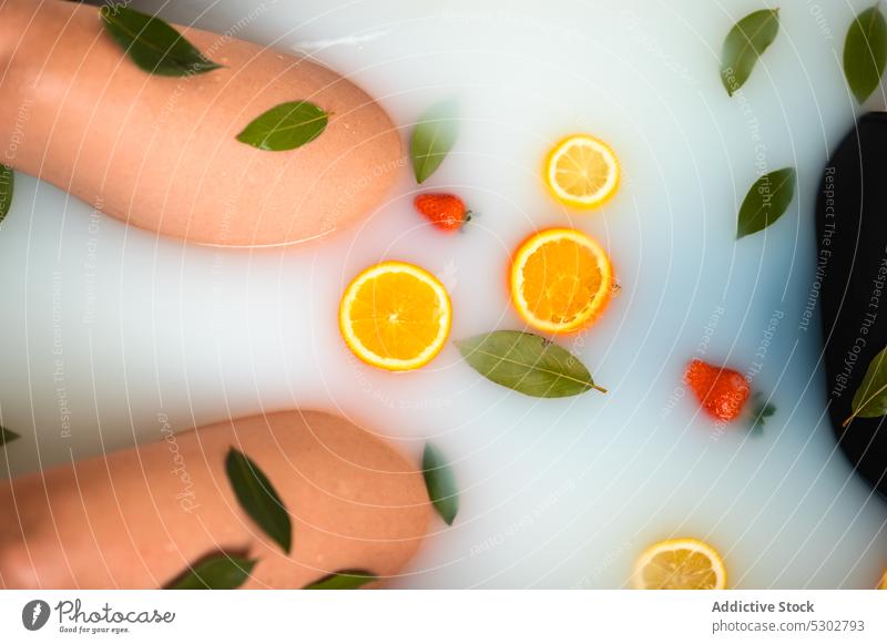 Crop woman taking milk bath with sliced oranges strawberries and leaves rejuvenate therapy hydrate leaf strawberry female treat healthy skin care peaceful