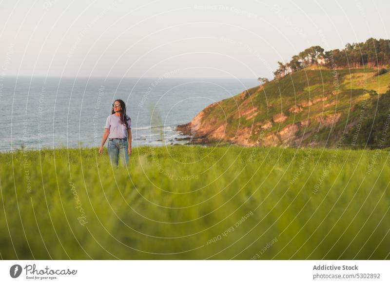 Happy woman walking on grassy hill near sea admire nature picturesque peaceful travel smile happy female casual sunglasses enjoy summer young freedom trip