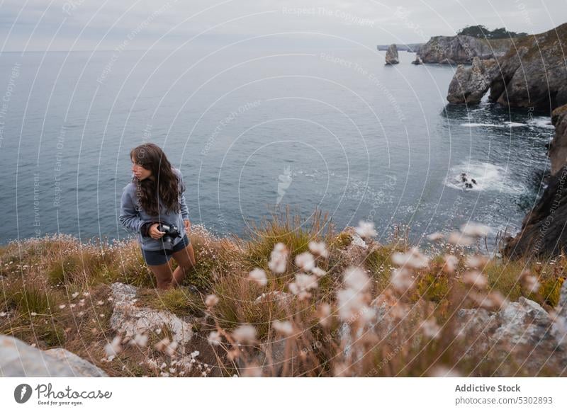 Female photographer standing on cliff against sea woman travel grassy professional photo camera horizon endless female young equipment daytime ocean daylight