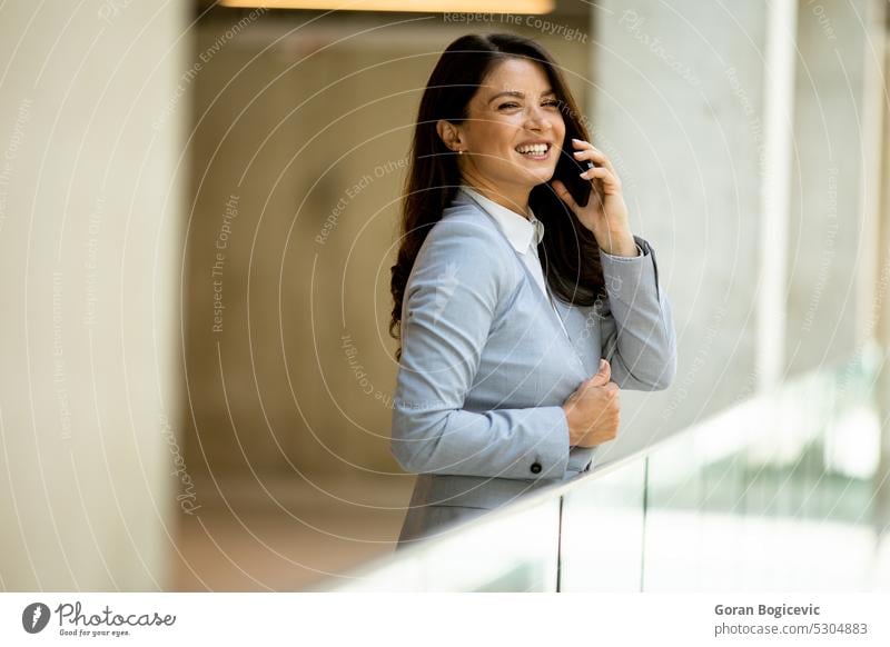 Young business woman using mobile phone in the office hallway caucasian professional businesswoman female people person confident talking cellphone