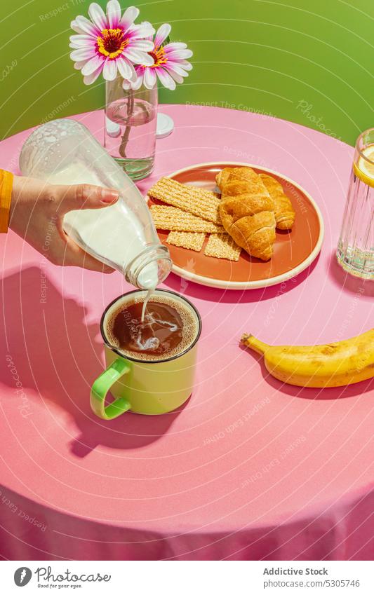 Crop person pouring milk into cup of coffee breakfast croissant beverage morning flower banana delicious cream fresh tasty drink vase sweet table pastry yummy