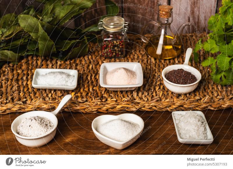 Small jars with different types of salt, black and pink from the Himalayas, normal, coarse, flakes, seasoned with truffle and from the Blackwater River (U.K.), accompanied by olive oil, pepper, bay leaf and parsley.