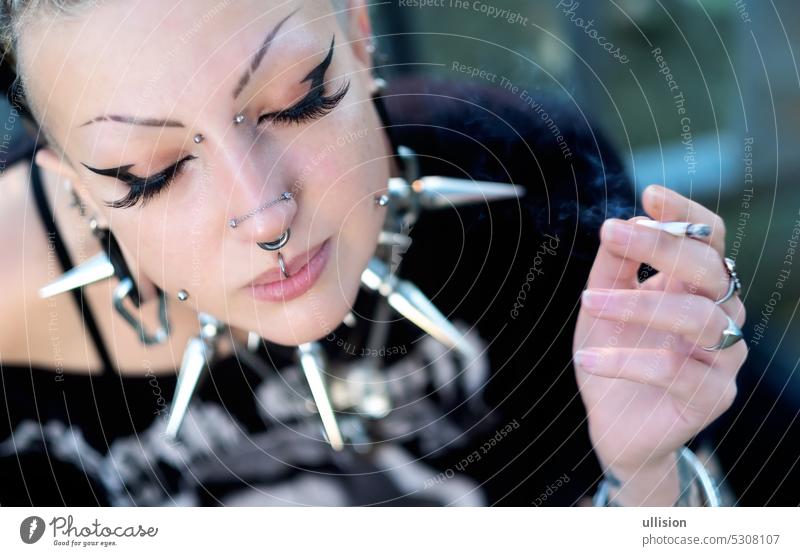 portrait of young sexy, seductive gothic girl with piercings, wearing a big spikes choker, with closed eyes and glued on artificial eyelashes smoking cigarette