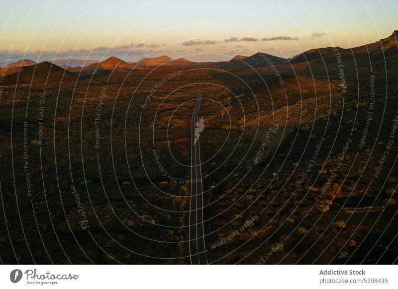 Drone view of roadway among rocky mountains at sundown sunset landscape valley nature range volcanic highland highway terrain wild rough ridge scenic