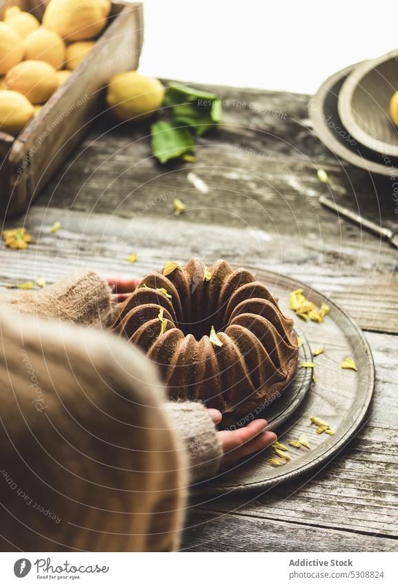 Anonymous person placing cake on wooden table lemon plate serve piece dessert kitchen at home lemon cake vegan cake plant-based box food tasty delicious fruit