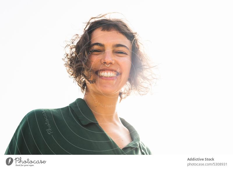 Cheerful woman with curly hair smiling at camera happy smile cheerful positive piercing short hair appearance personality trendy young bright content delight